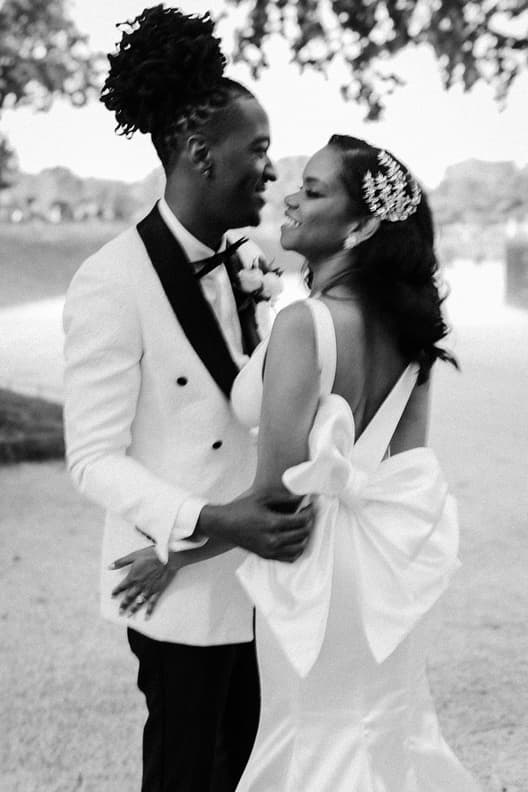 Bride and groom embrace by the Seine in soft light, her gown tied with a dramatic back bow