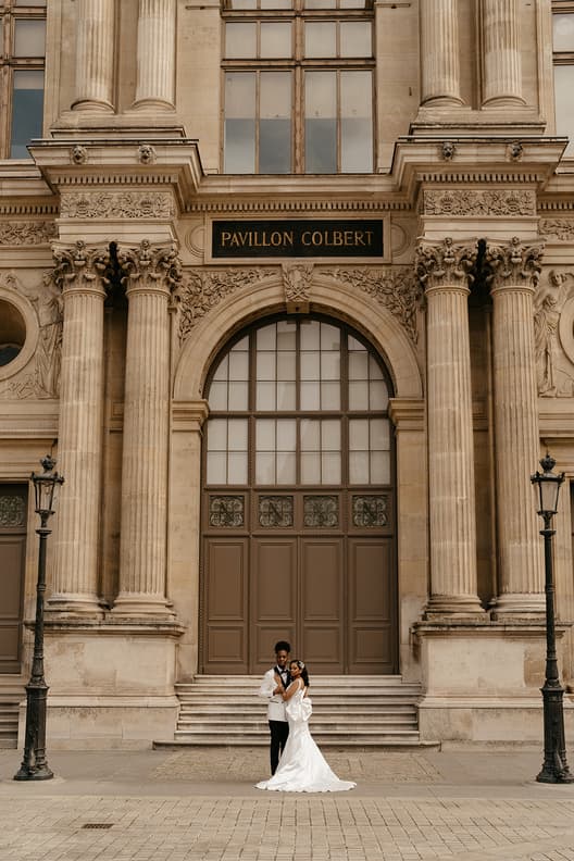 Bride and groom pose on the steps of Pavillon Colbert beneath warm daylight and stone columns