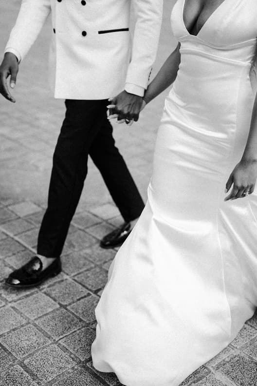 Bride and groom hold hands while walking on a Paris street in soft black-and-white light