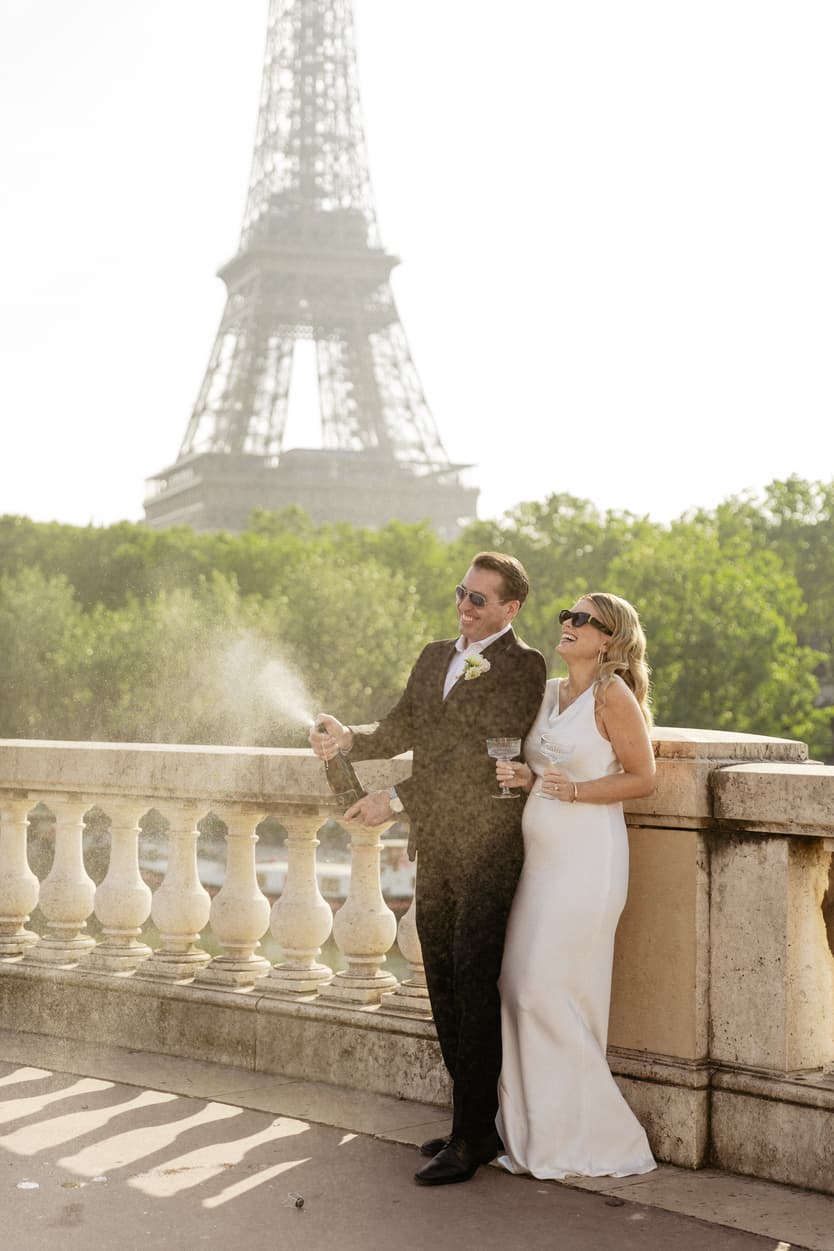 Bride and groom toast by the Eiffel Tower in warm light, champagne mist rising