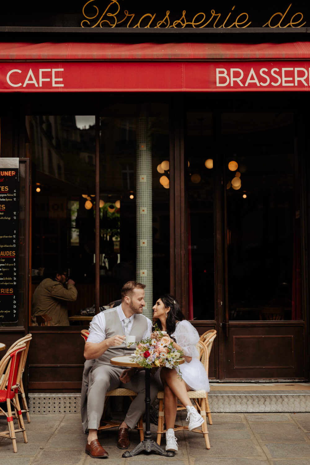 Bride and groom laughing while drinking coffee in a Parisian cafe
Bouquet of flower on the table