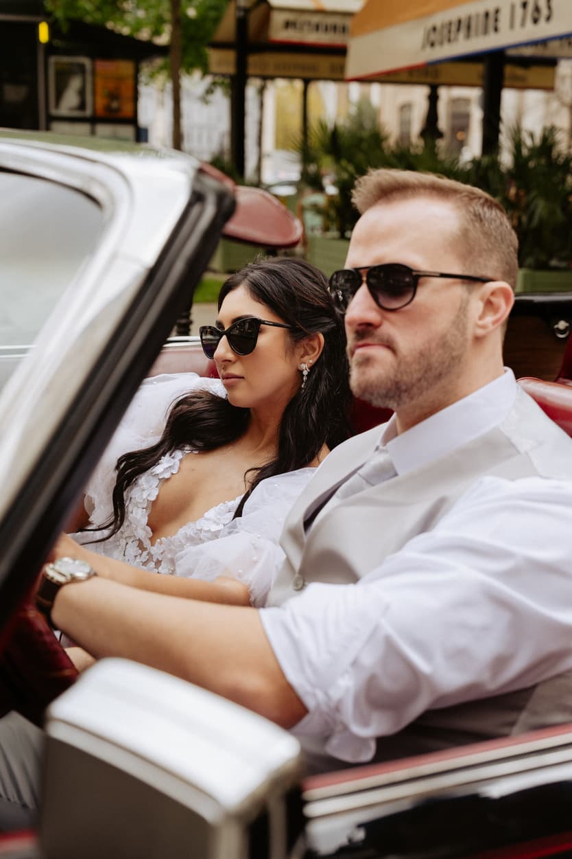 Bride and groom in sunglasses ride a vintage convertible on a Paris street in soft daylight