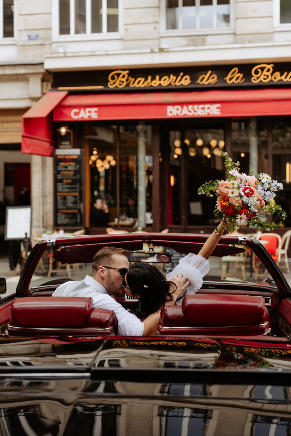 Bride and groom kissing in a vintage car while the bride holding up a colorful bouquet of flowers