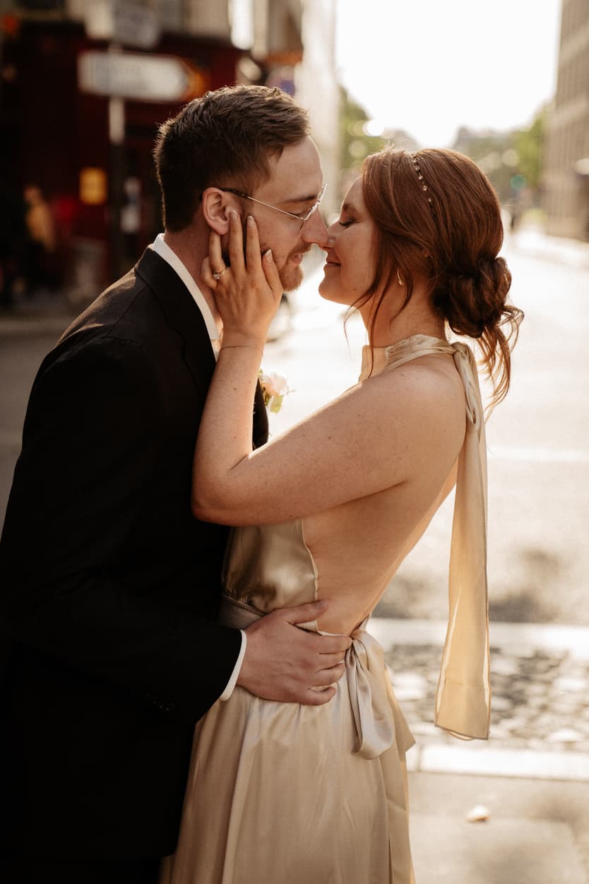 Bride and groom embrace on a sunlit Paris street, foreheads touching in warm backlight