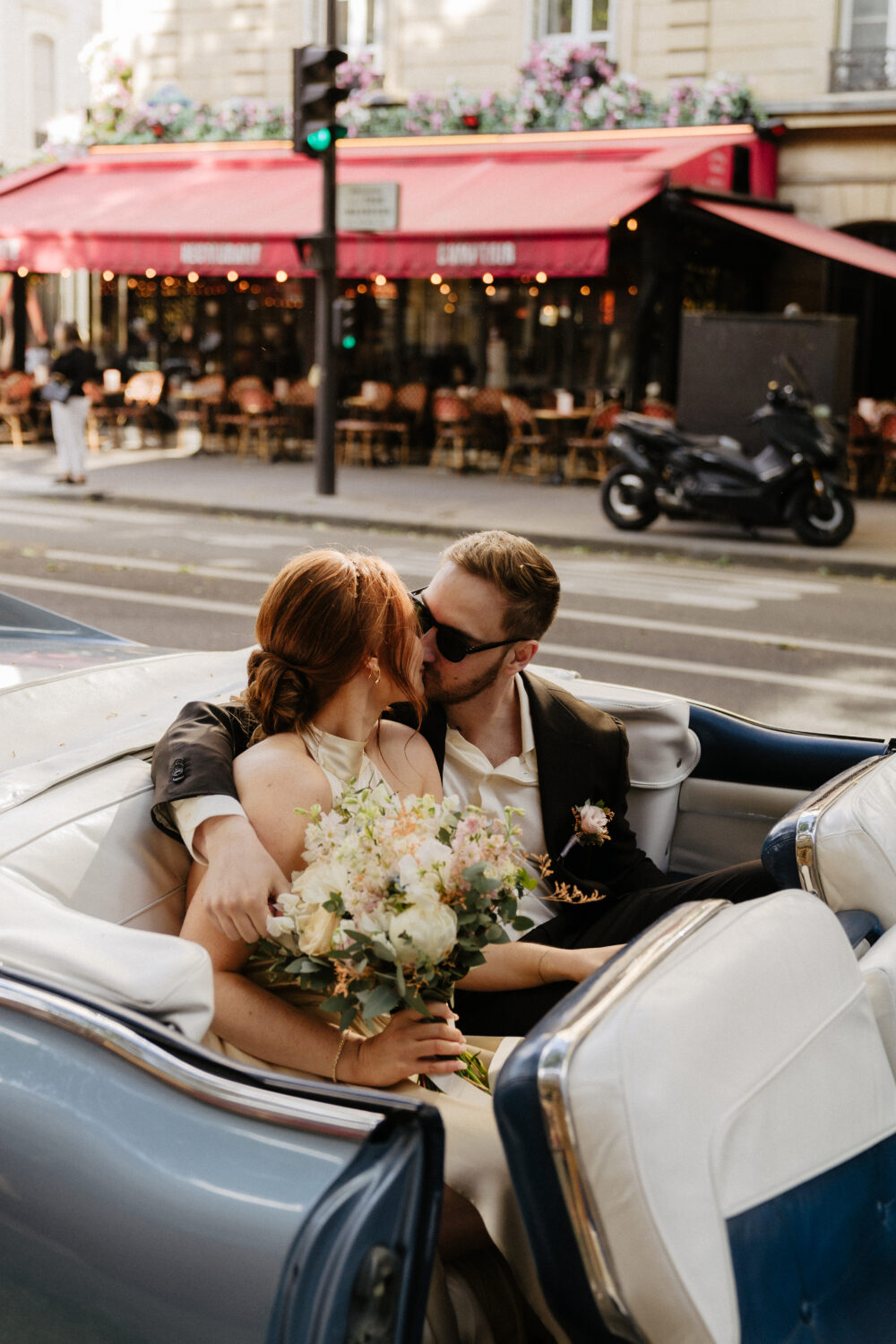 paris elopement couple kissing in a blue vintage car with a café behind