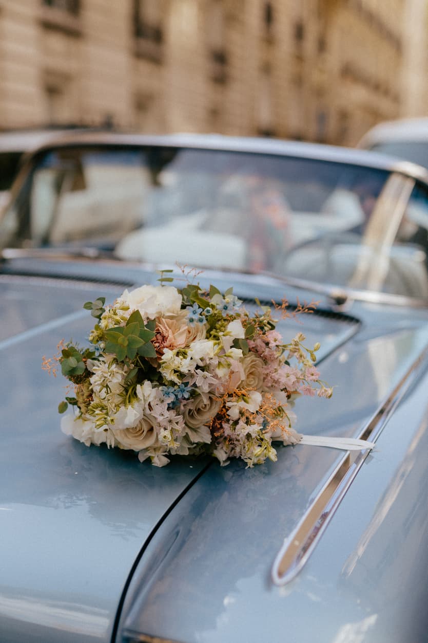 Bouquet of pastel flowers rests on a vintage blue car on a Paris street in soft daylight