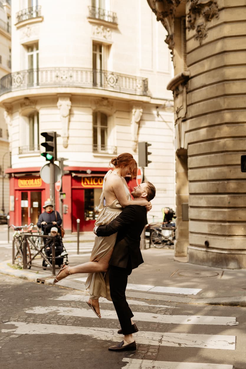 Bride and groom kiss and lift on a Paris street in warm light beside a corner café