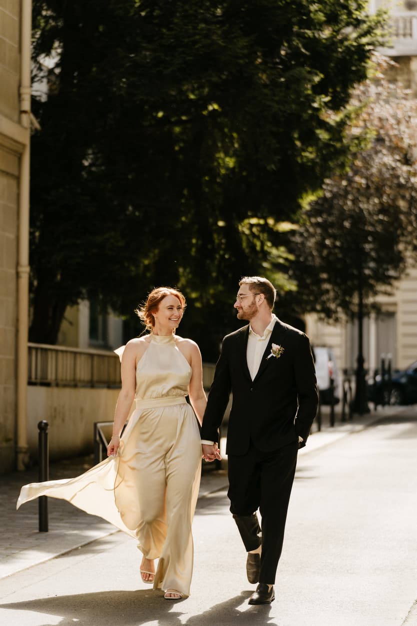 Bride and groom walk hand in hand on a Paris street in warm golden light