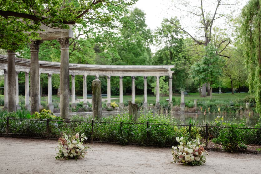 Soft daylight over a Paris garden with a stone colonnade, pond, and floral arrangements