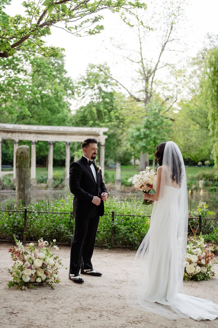 Bride and groom face each other in a Paris garden, framed by flowers and soft daylight