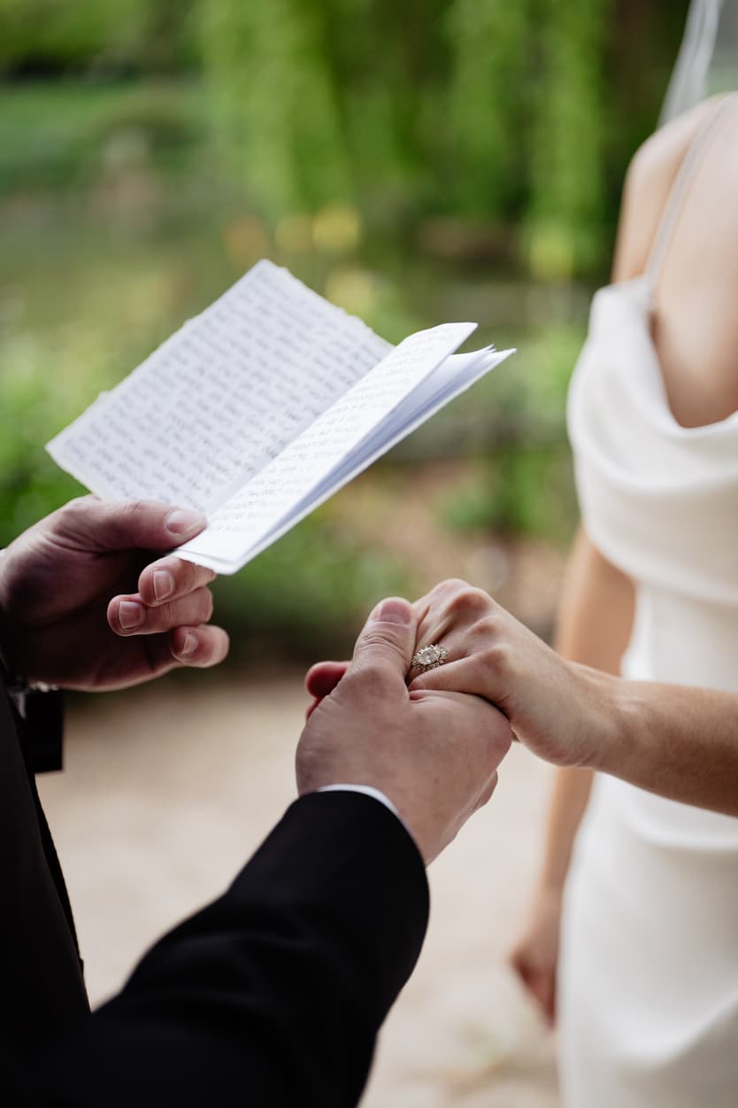A groom holding his handwritten vows as he takes his bride’s hand