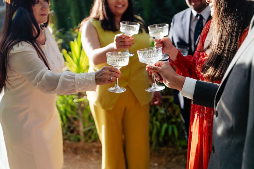 Guests in colorful attire toast with coupe glasses in a sunlit Paris garden