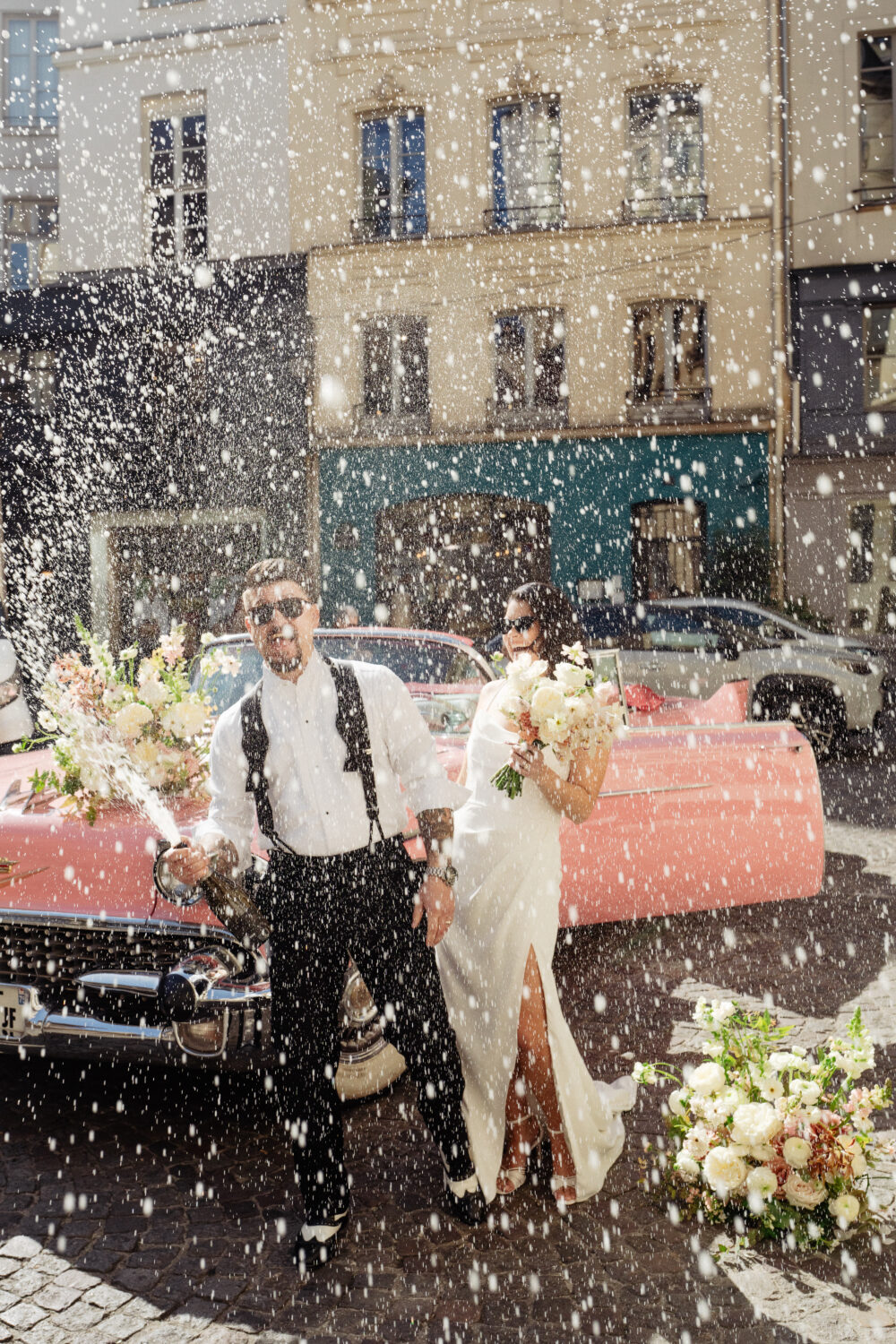 Champagne shower during an elopement in Paris with pink vintage car behind them