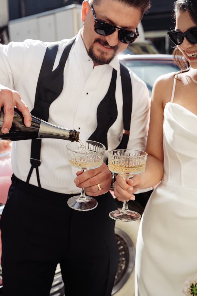 Bride and groom in sunglasses pour champagne on a Paris street in bright afternoon light