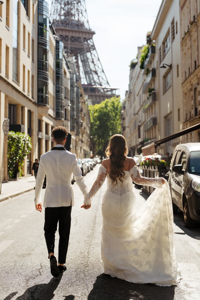Bride and groom walk hand in hand down a Paris street, with the Eiffel Tower rising ahead