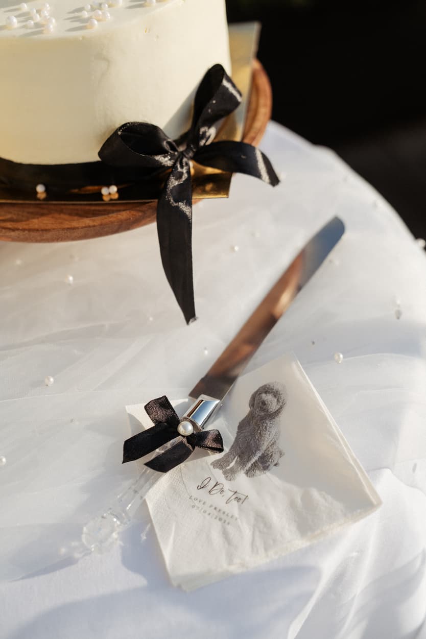 Wedding cake details in warm light, with a black ribbon, pearl accents and a satin knife handle