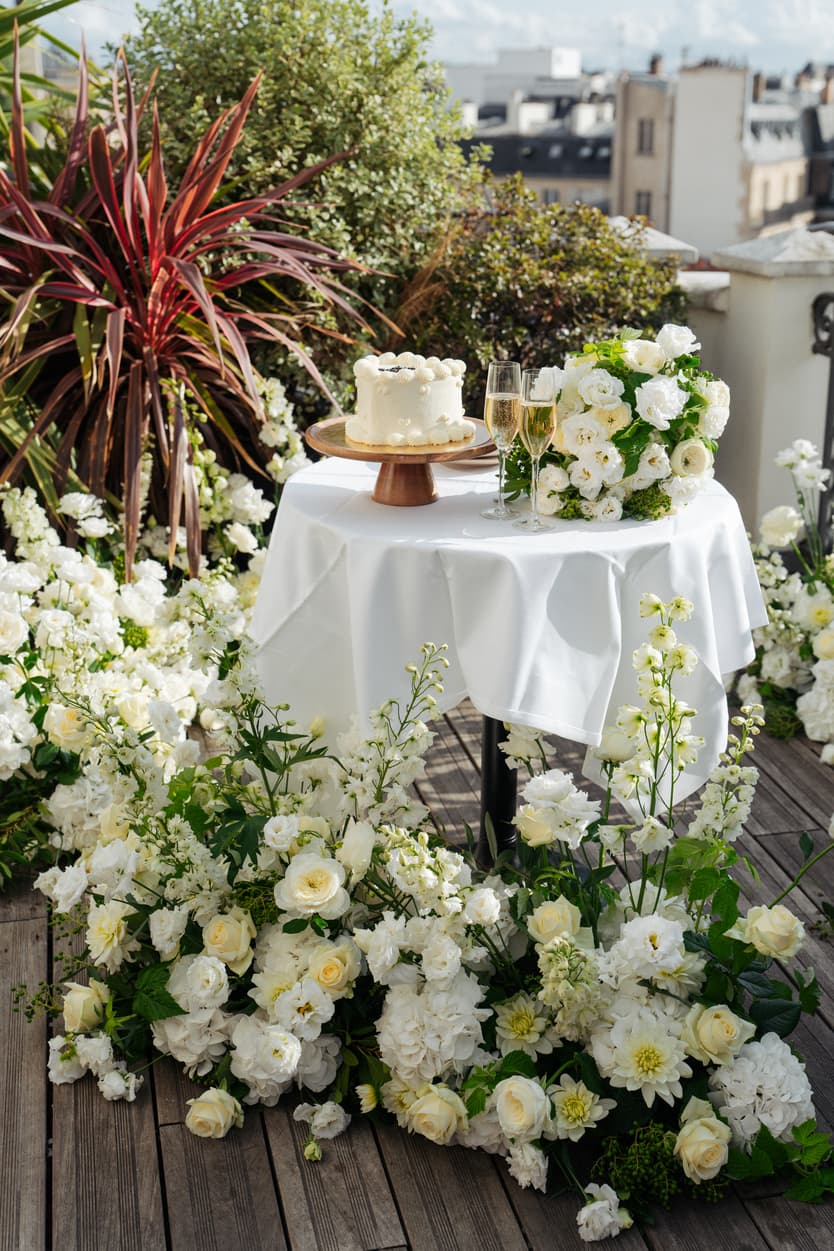 White cake, champagne and flowers in bright sunlight on a rooftop terrace with Paris rooftops