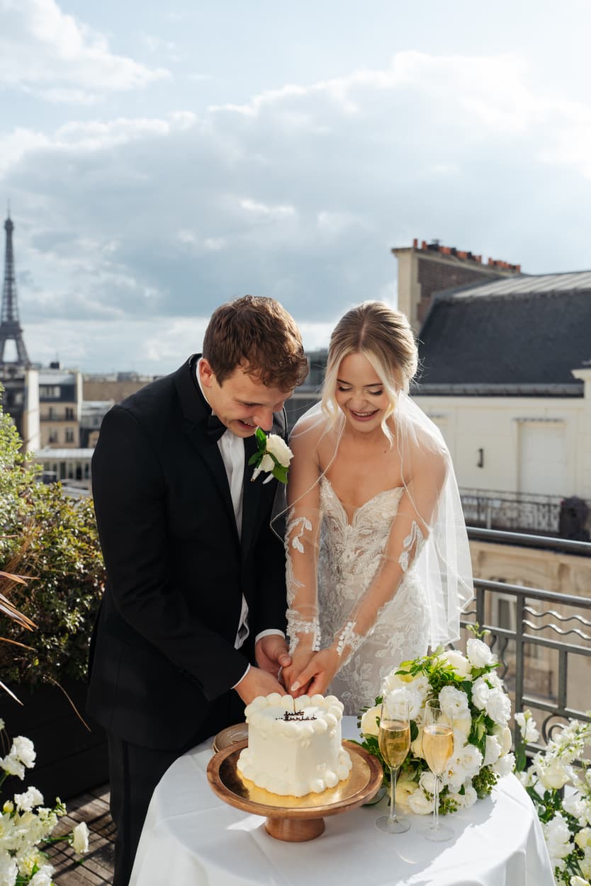 Newlyweds cut their wedding cake on a Paris rooftop terrace with the Eiffel Tower in soft daylight