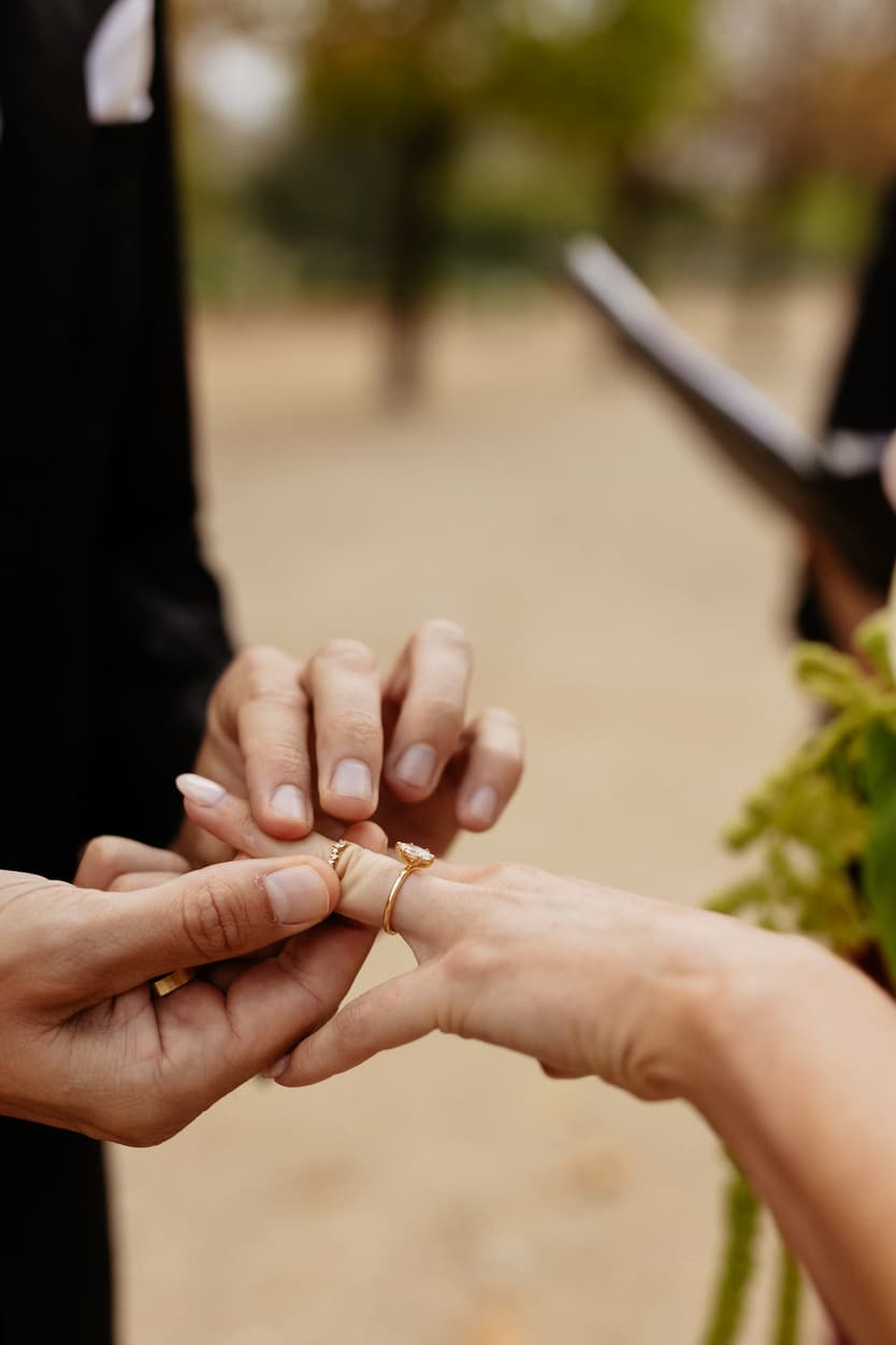 Hands place a gold ring on the bride’s finger during an outdoor garden ceremony