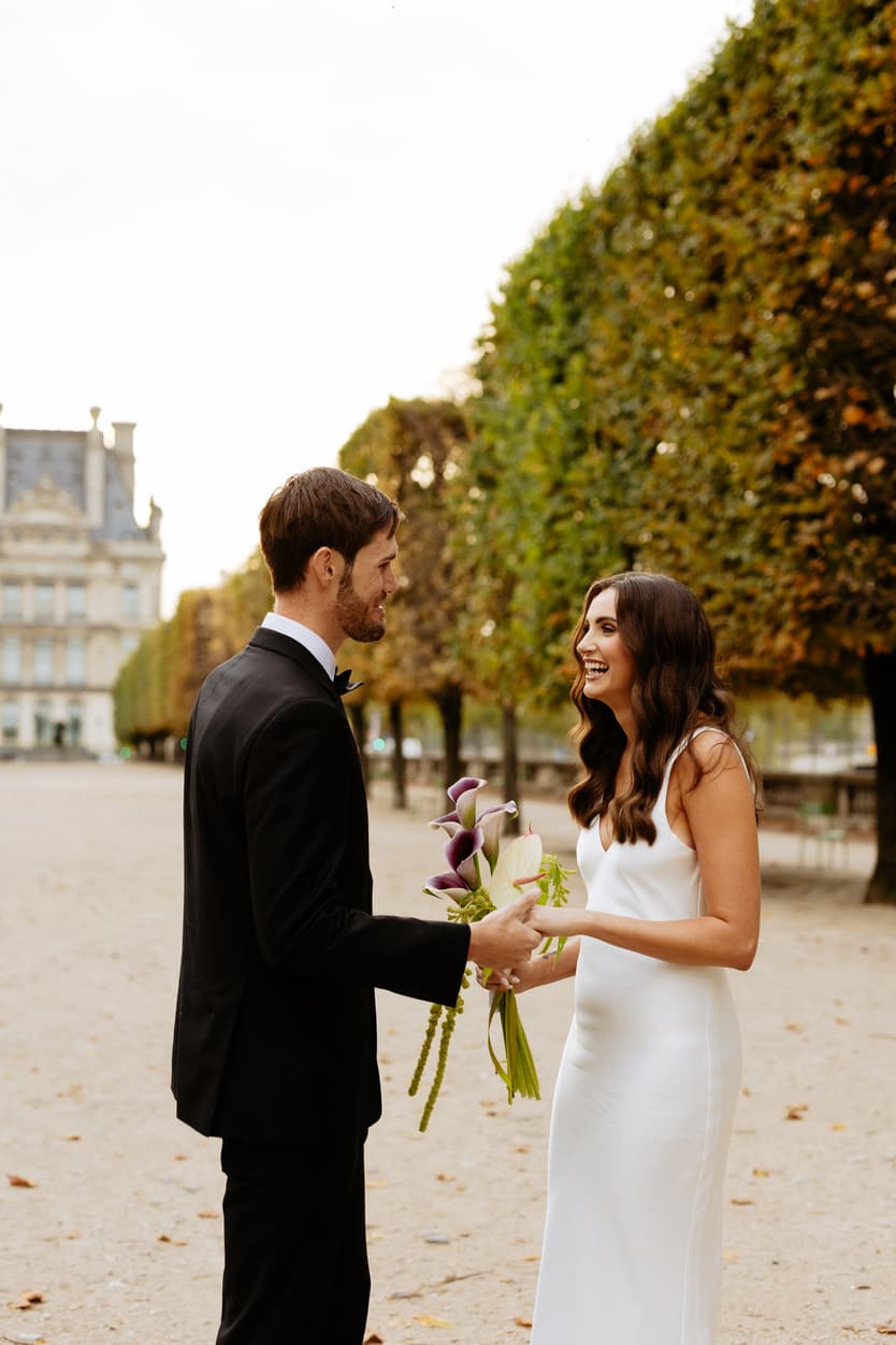 Bride and groom exchange a bouquet on a tree-lined Paris path in warm evening light