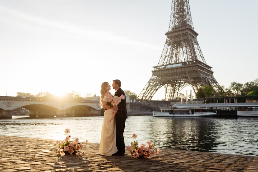 Bride and groom embrace by the Seine at sunset with the Eiffel Tower rising behind them