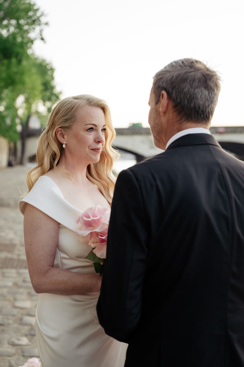 Bride holding pink bouquet faces groom on a Paris street in soft evening light