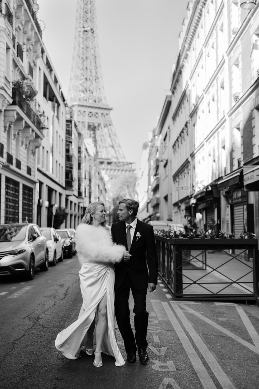 Bride and groom walk arm in arm on a Paris street with the Eiffel Tower rising behind them