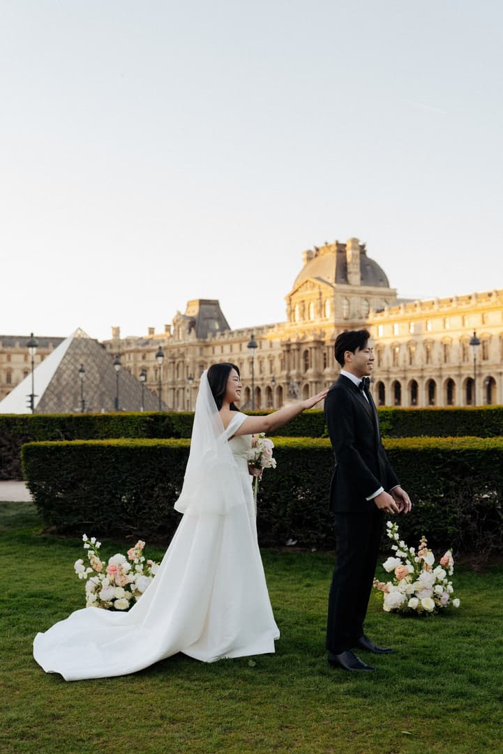 Nancy taps Jason on the shoulder for their first look in front of the Louvre at sunrise
