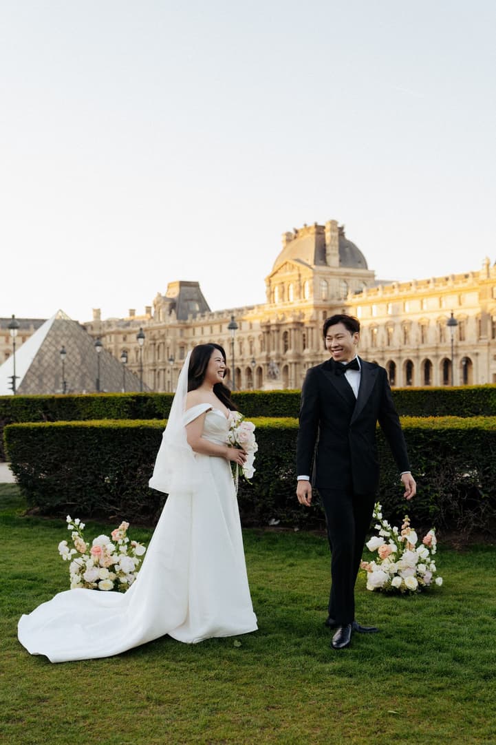 Jason turns around grinning at his first look at Nancy in front of the Louvre at sunrise