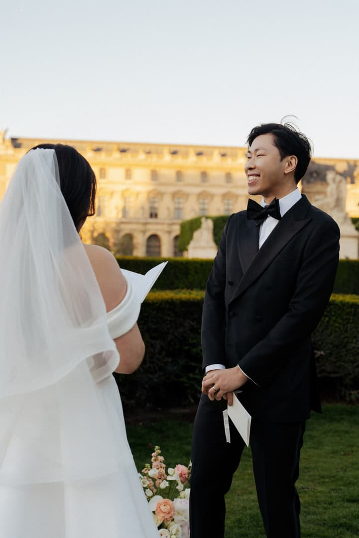 Jason laughing as Nancy reads her vows in the garden in front of the Louvre