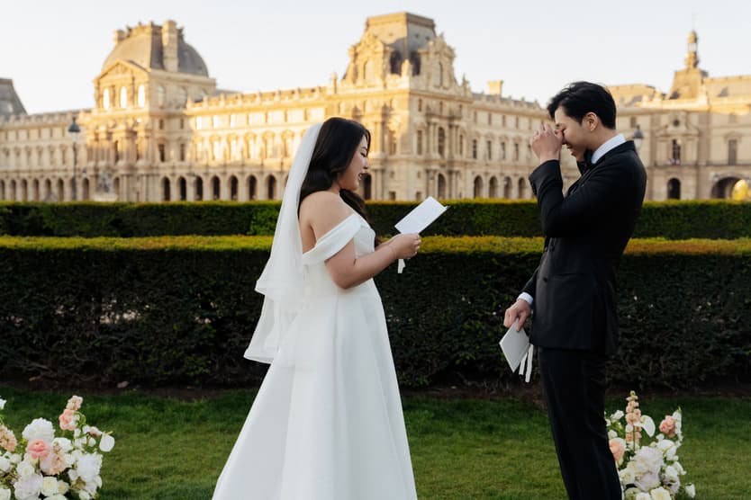 Jason covering his face with emotion as Nancy reads her vows in front of the Louvre