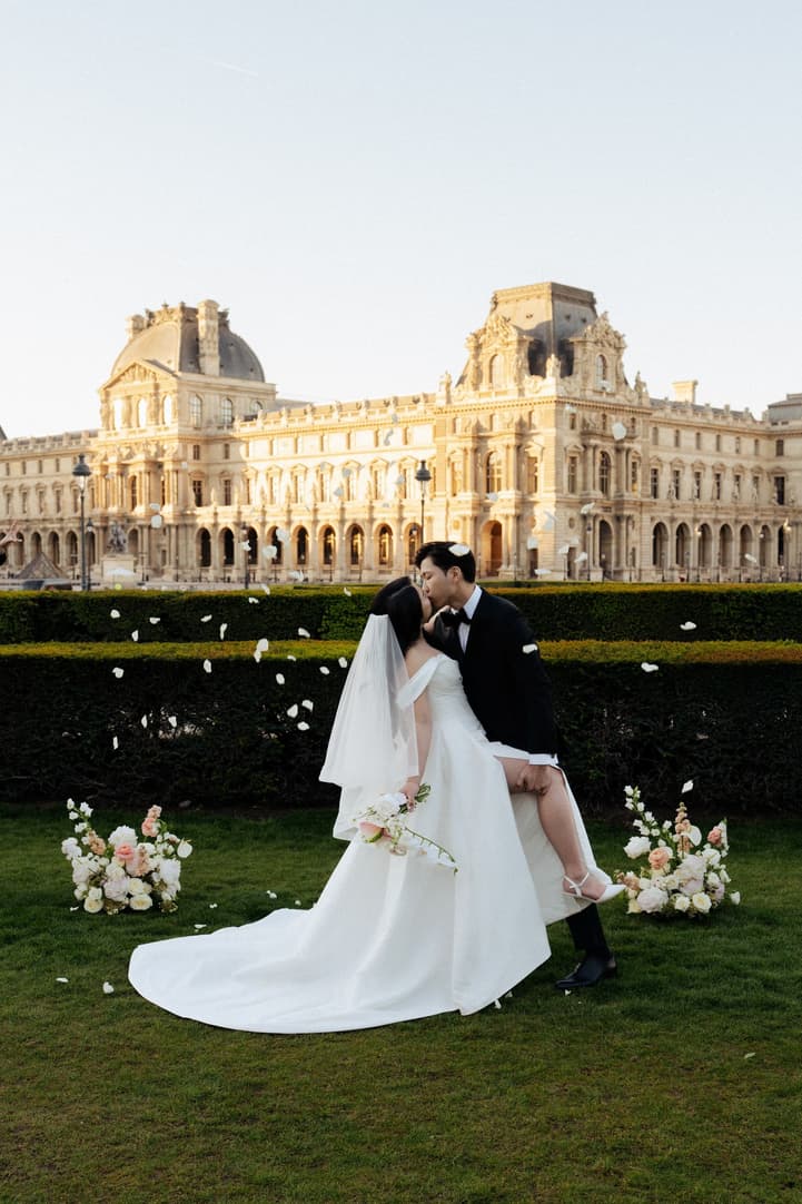 Jason dipping Nancy for a kiss under falling petals in front of the Louvre