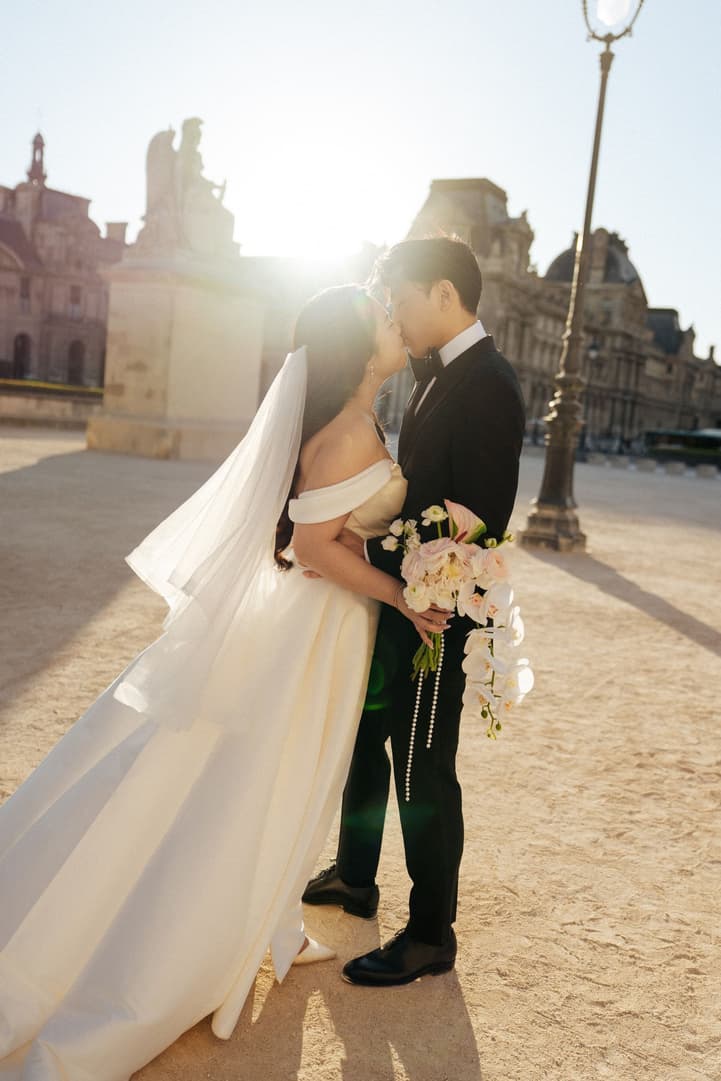 Jason kissing Nancy in the sunrise light of the Louvre courtyard