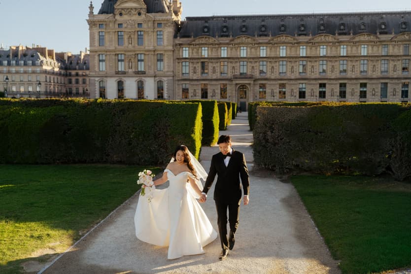 Nancy and Jason walking hand in hand along a garden path by the Louvre