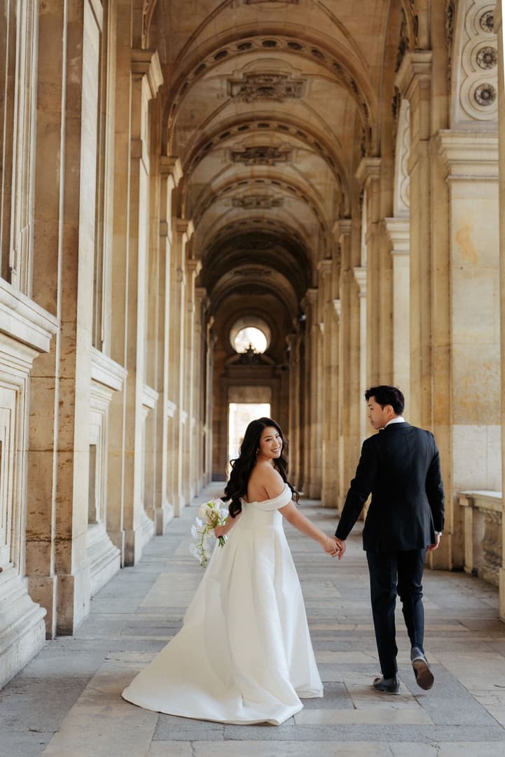 Nancy looking back over her shoulder as she walks with Jason through the hallway of the Louvre