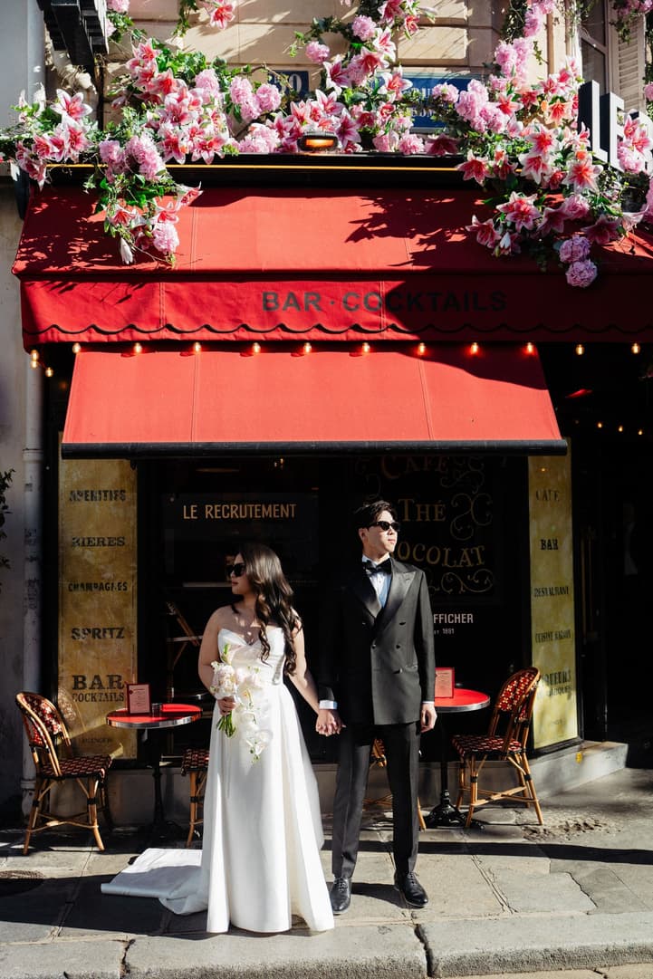 Nancy and Jason in front of a red-awning Paris café covered in pink flowers