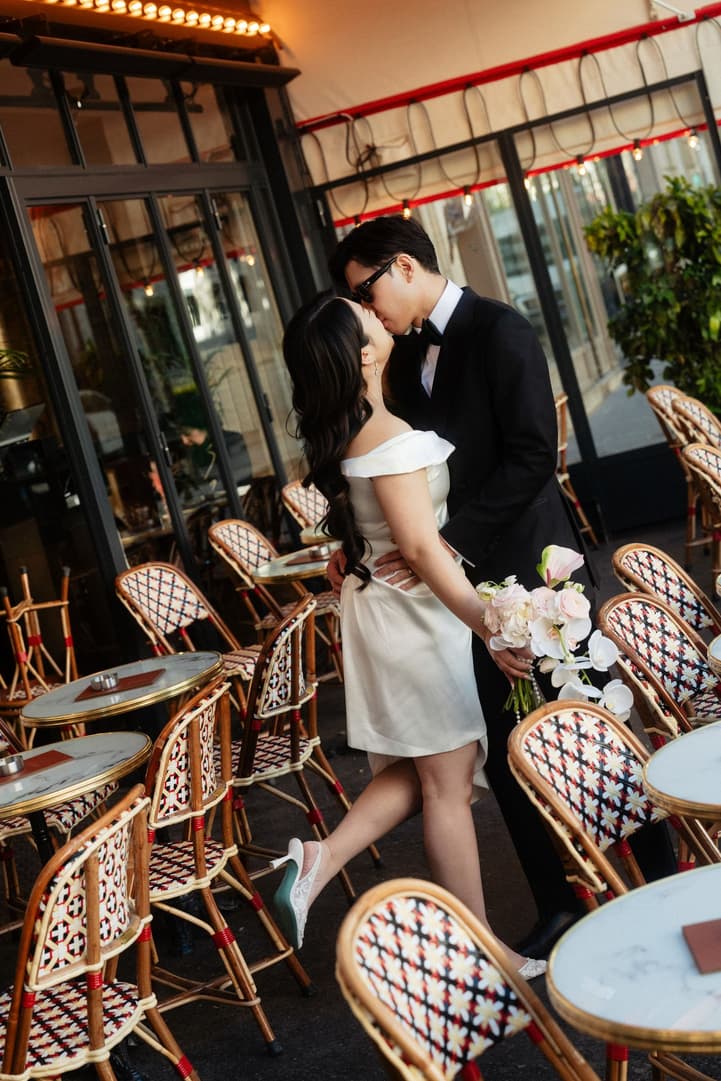 Nancy and Jason kissing among the rattan chairs of a Paris café terrace