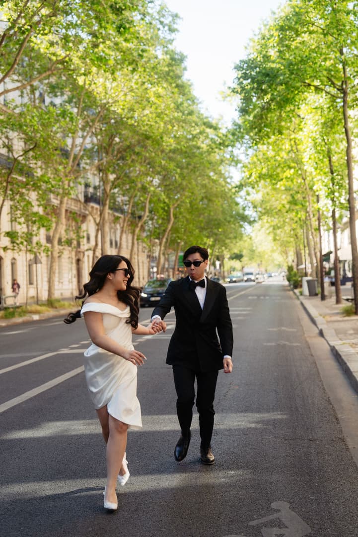 Nancy and Jason running hand in hand down a tree-lined Paris avenue