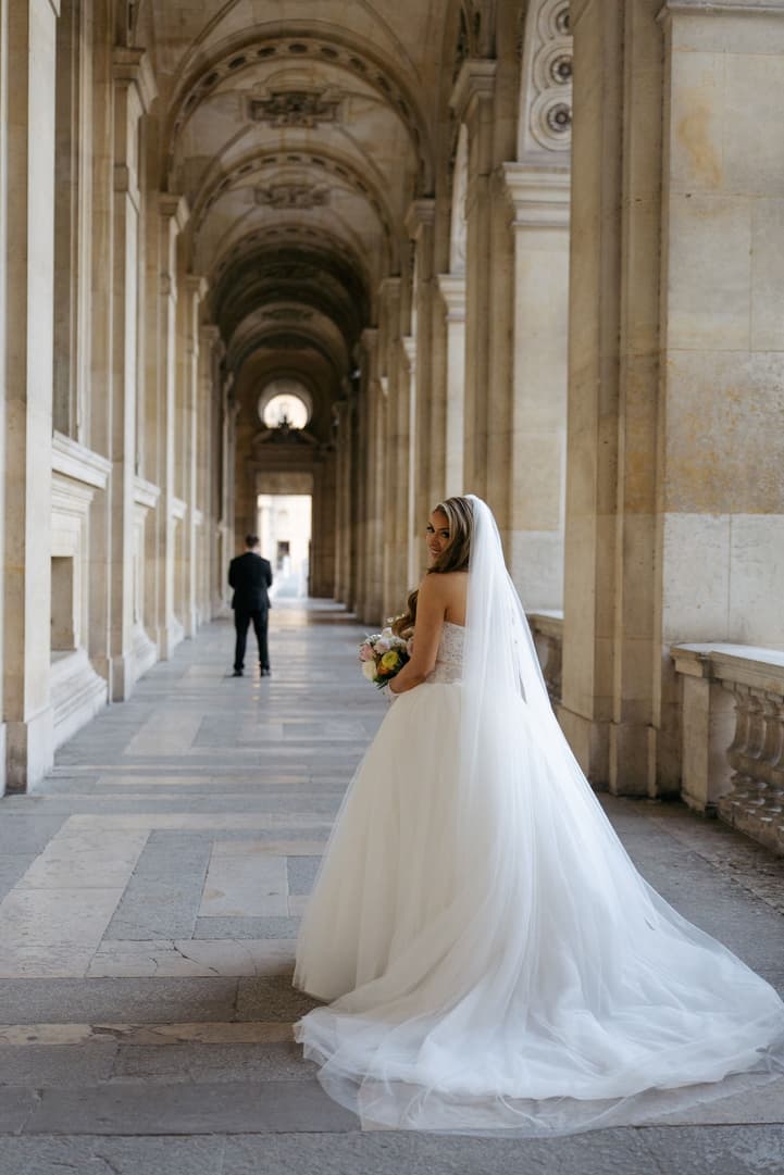 Aphrodite walking up behind Michael in the hallway of the Louvre for their first look