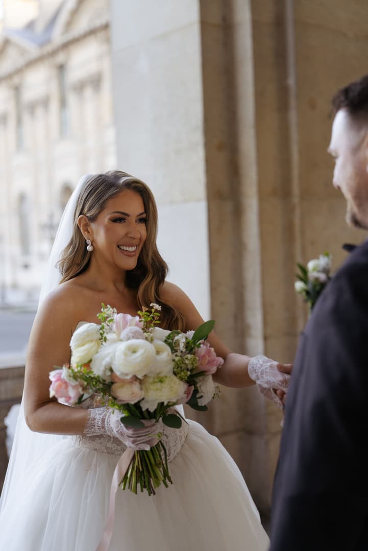 Aphrodite smiling with her bouquet and lace gloves at her first look in Paris
