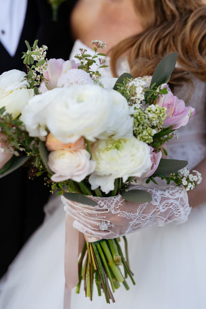Aphrodite's bridal bouquet of white ranunculus and pink tulips held in a lace glove