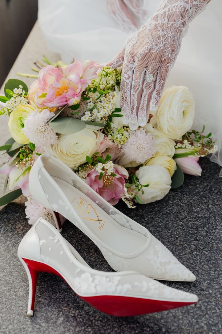 Aphrodite's lace-gloved hand on her bouquet beside her wedding shoes