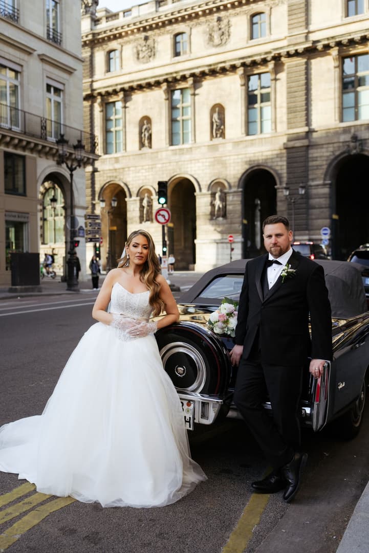 Aphrodite and Michael beside a black vintage convertible in front of the Louvre