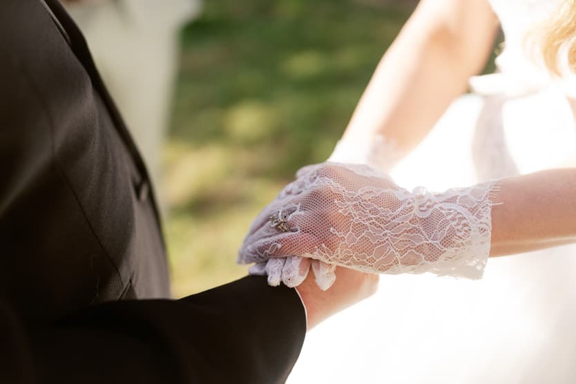 Michael holding Aphrodite's lace-gloved hand during the ceremony