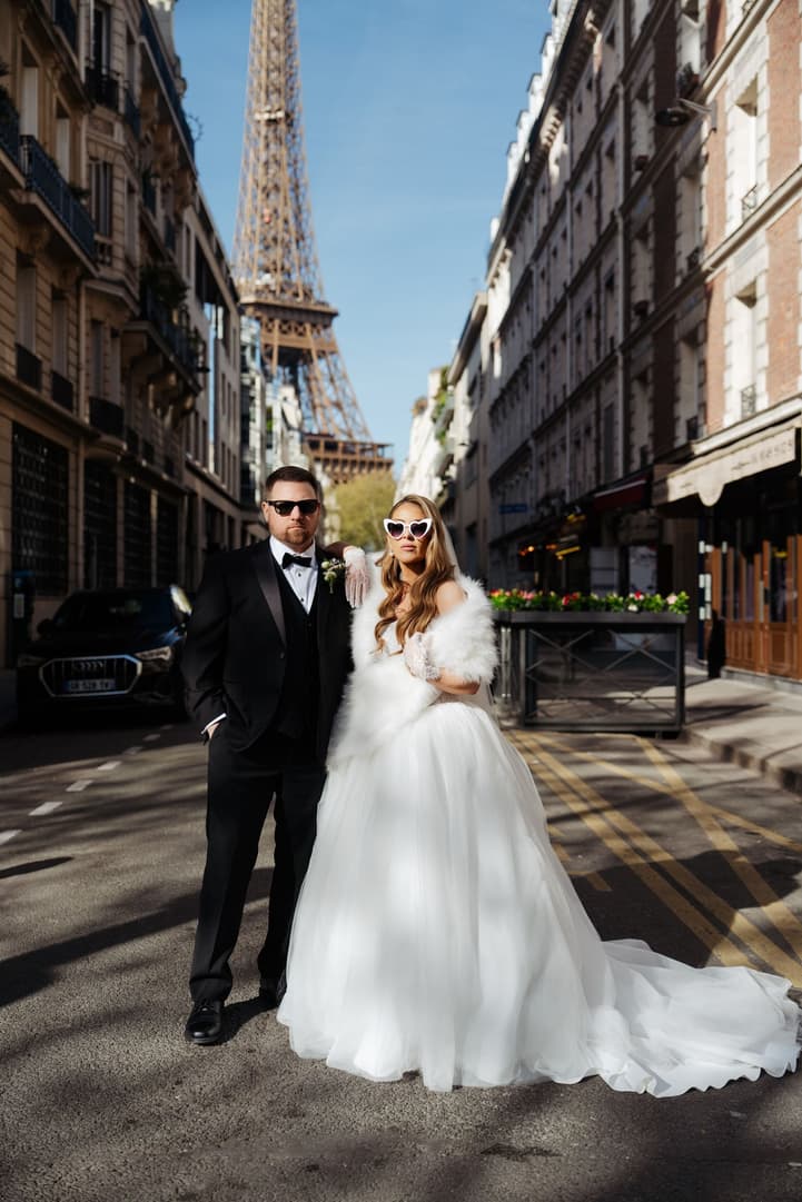Aphrodite and Michael in sunglasses on a street with the Eiffel Tower behind