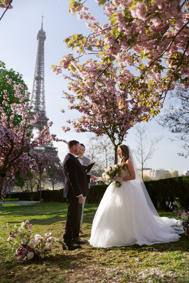Aphrodite and Michael facing each other under the cherry blossoms, the Eiffel Tower behind