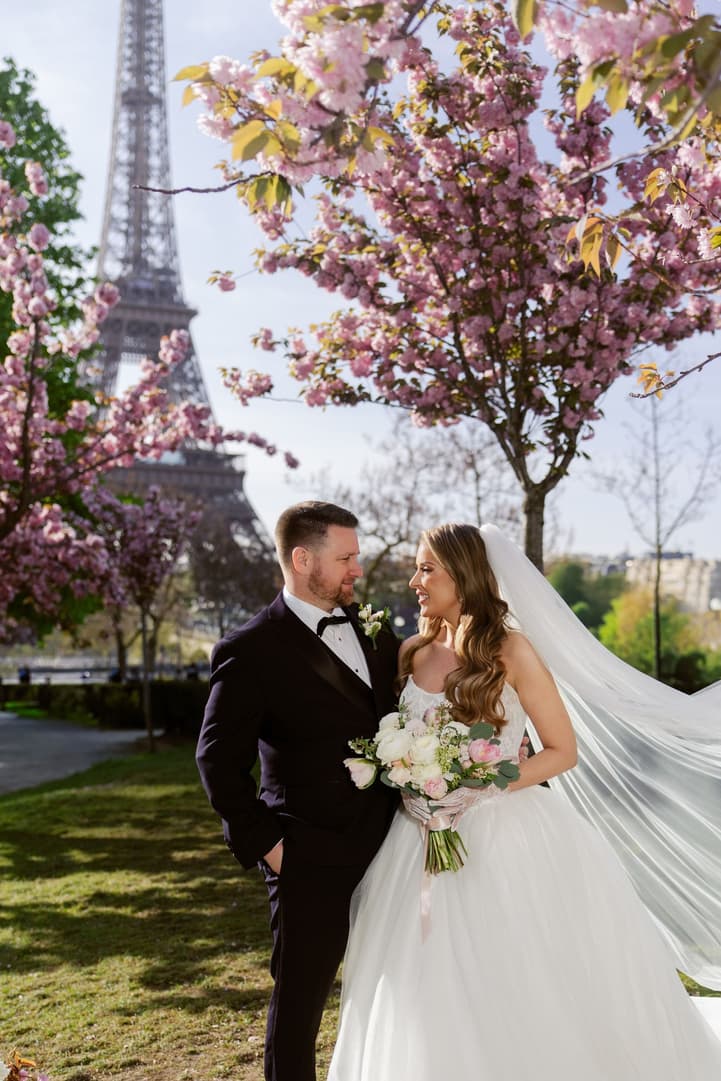 Aphrodite and Michael smiling under the cherry blossoms, her veil in the wind