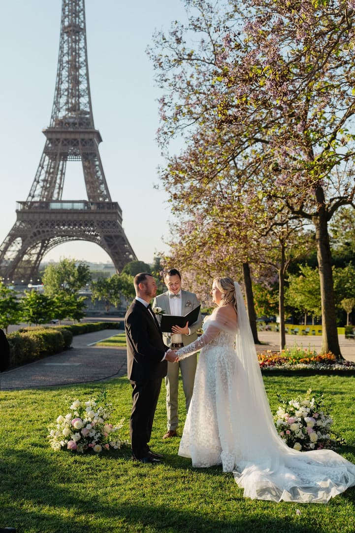 Victoria and Tyler before their officiant in the Trocadéro gardens, flowers on the lawn and the Eiffel Tower behind