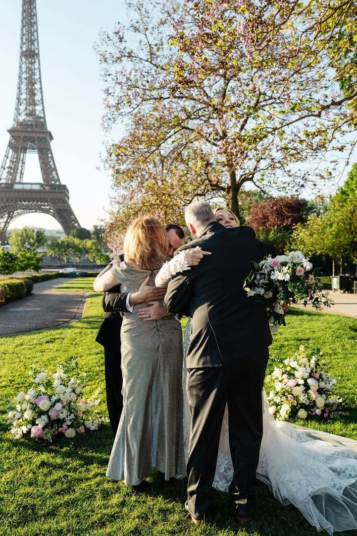 Their family embraces the newlyweds by the ceremony flowers in the Trocadéro gardens