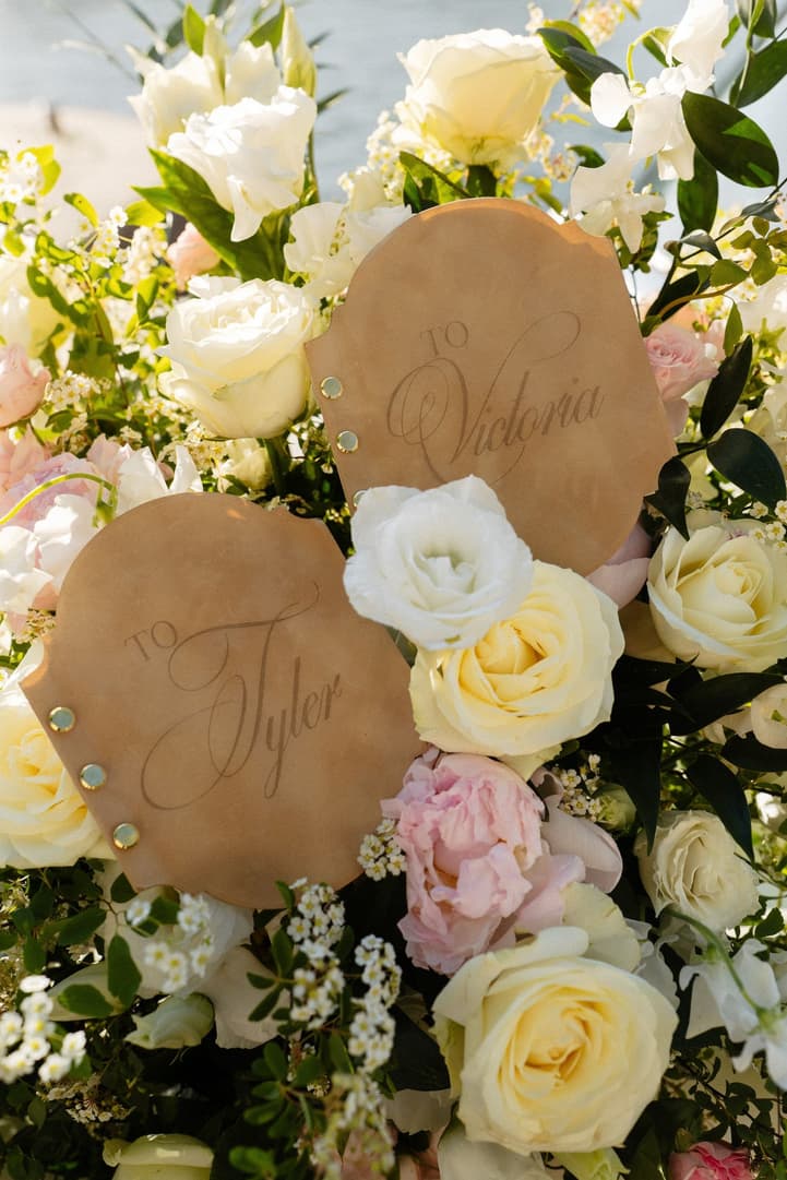 Victoria and Tyler's vow books, their names written on them, among white, ivory and pale pink roses
